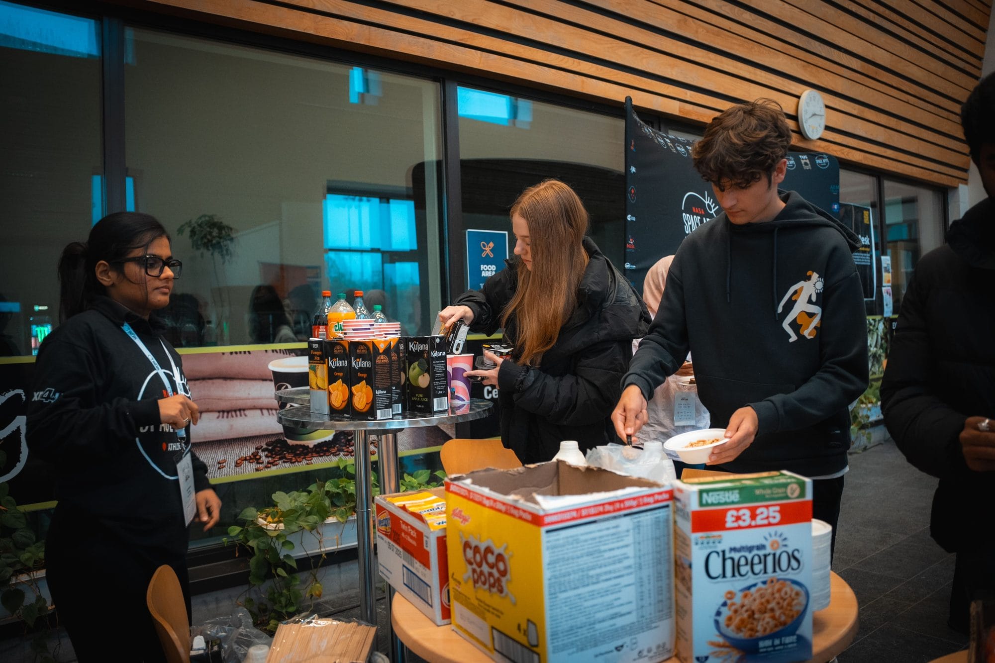 A crew member at the breakfast table as participants help themselves to cereal and juice at HackAthlone 2025