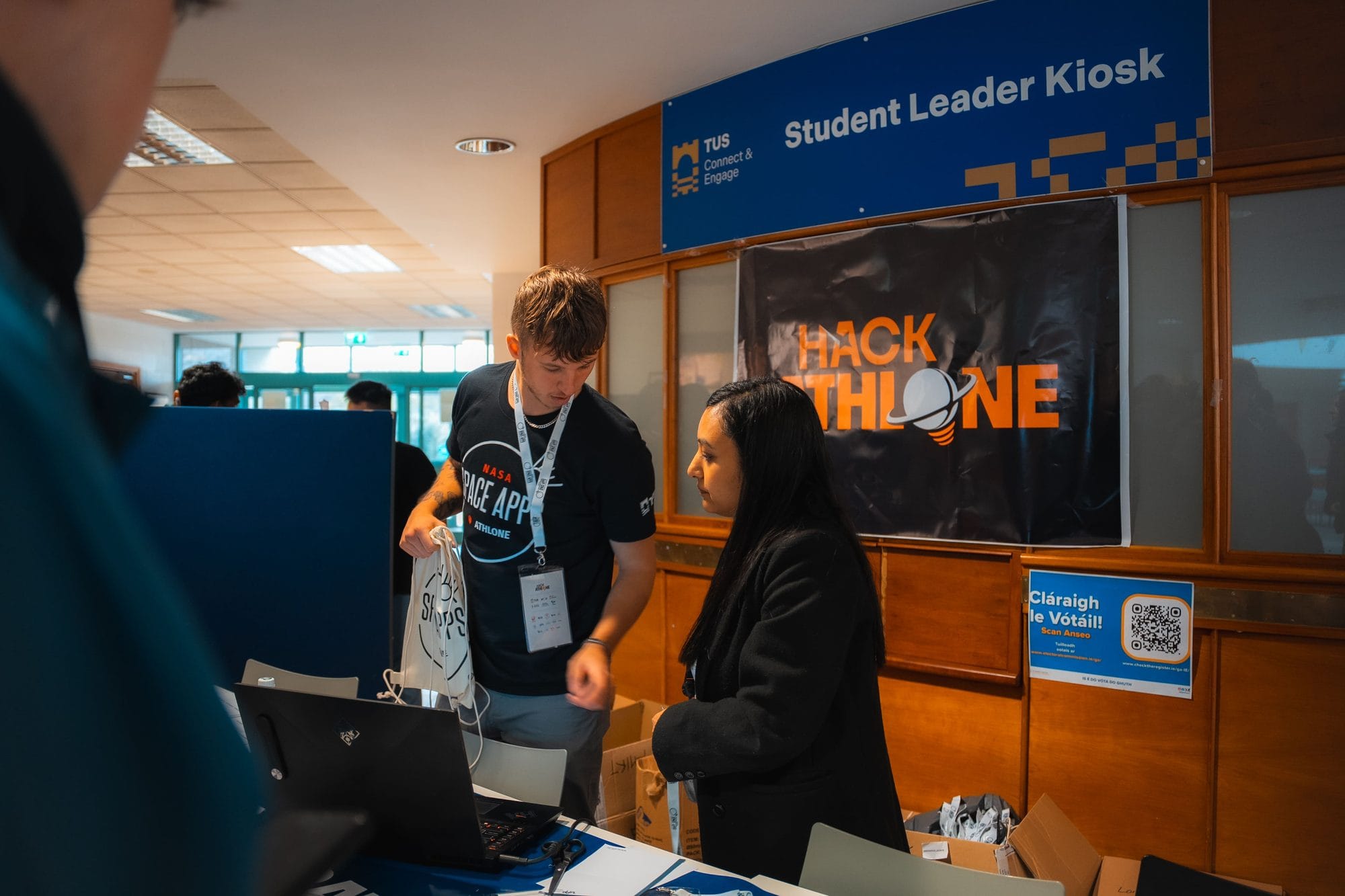 A crew member in a NASA Space Apps Athlone T-shirt packs a Space Apps bag at the HackAthlone registration point in 2025