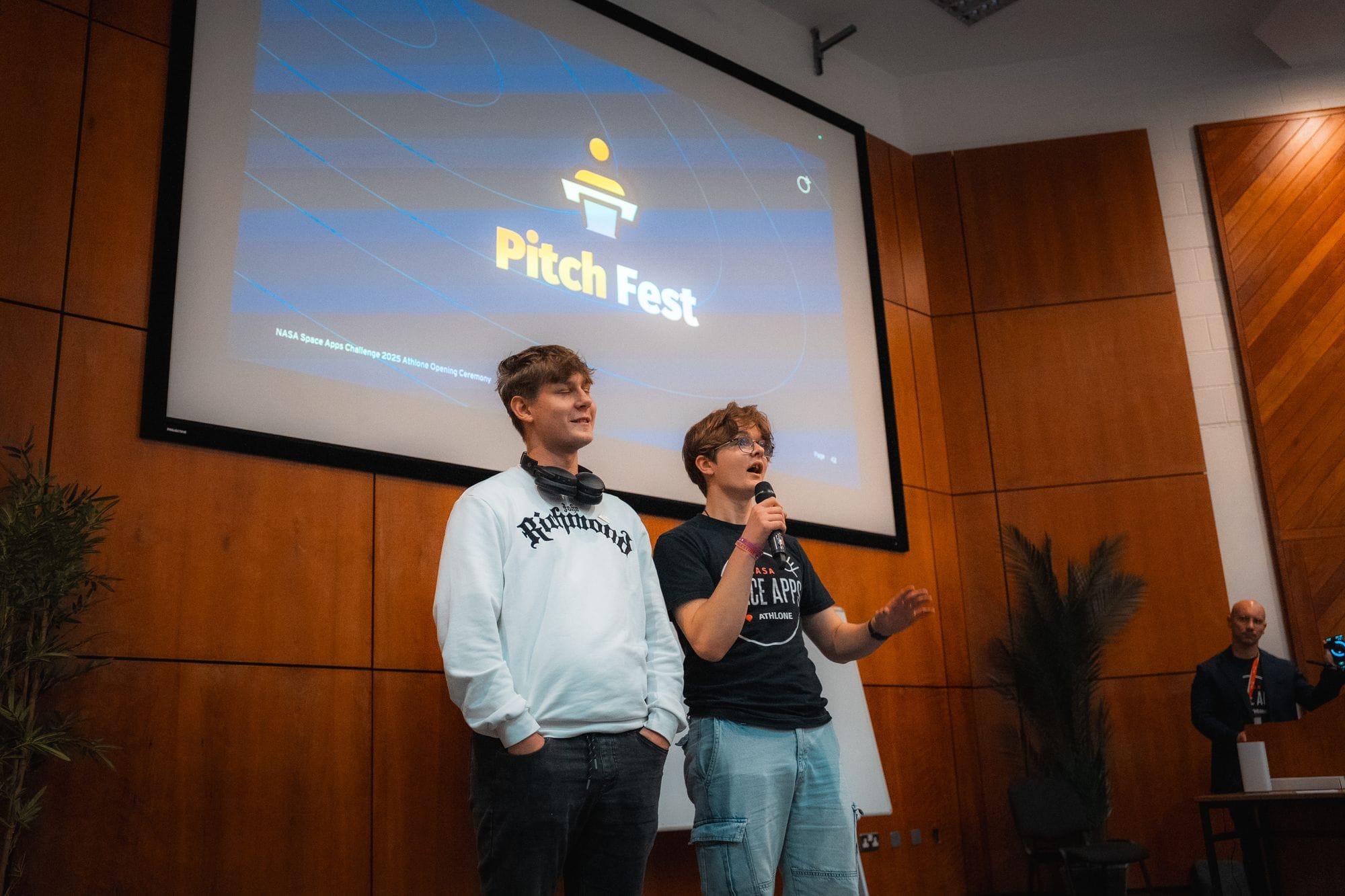 Two participants pitching an idea on stage in front of a Pitch Fest slide